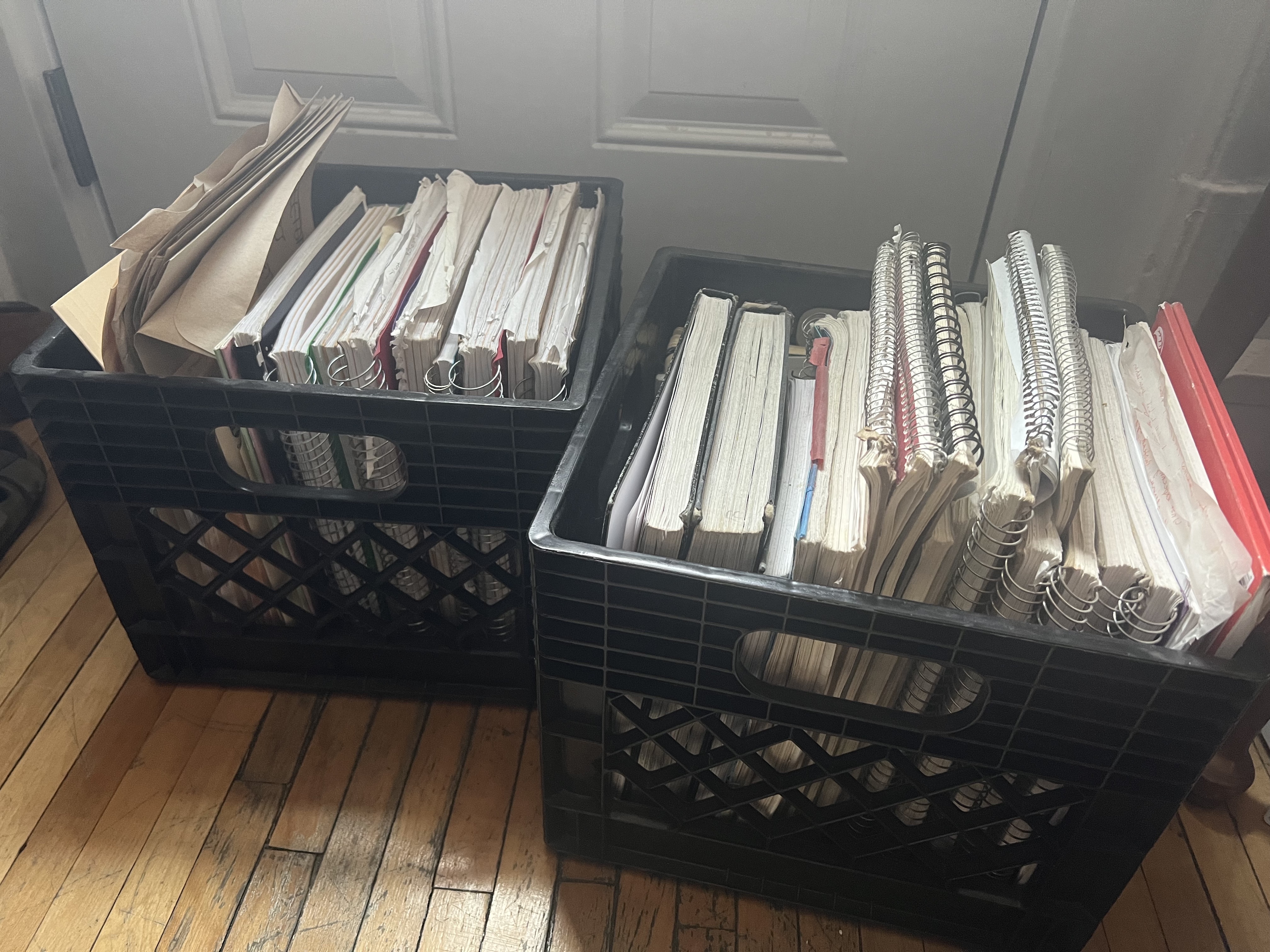 A photograph of two black milk crates stuffed full of notebooks, looseleaf paper, and manilla folders.